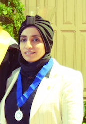 Hadeel M. Alawad - Taken indoors. Hadeel, wearing a black hajib, black top with a white blazer, and a recognition medal (from the Honor Society of Phi Kappa Phi) with a royal blue ribbon around her neck, is smiling at the camera.